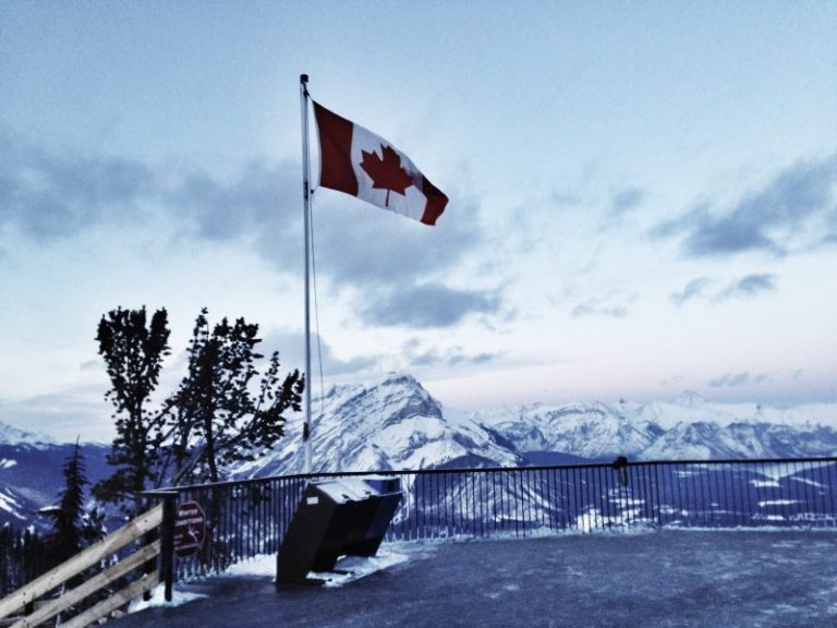 Canadian flag on a pole overlooking snowy mountains