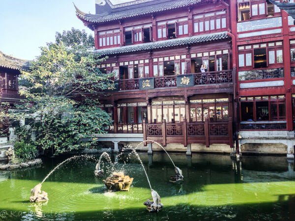 green pond with a fountain in front of a chinese style building