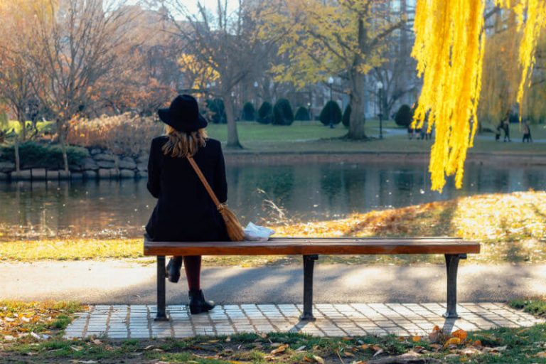 a woman sitting on a bench in a park with leaves falling 