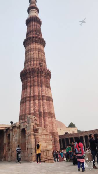 brick tower Qutub Minar with airplane in the sky