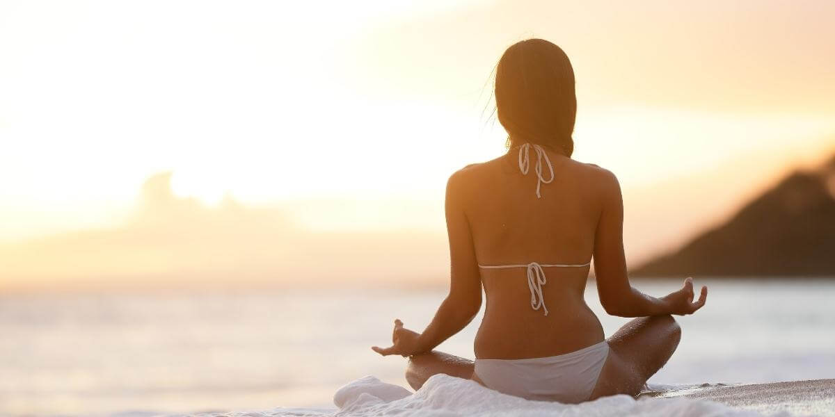 wellness travel - woman doing yoga on the beach